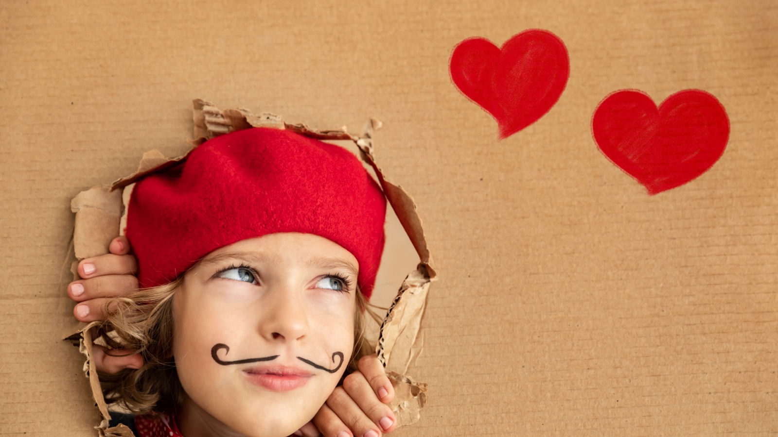 Niña jugando con un sombrero de personaje y corazones dibujados